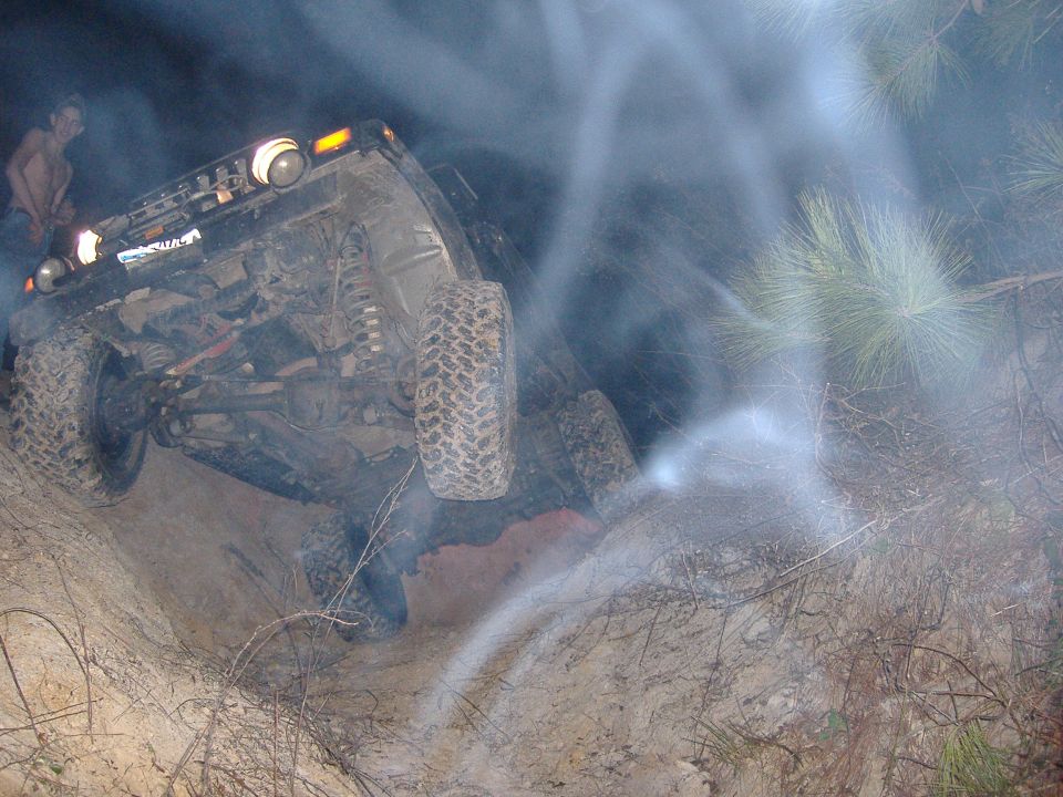 2004 Jeep Wrangler on its side in dirt with smoke around it