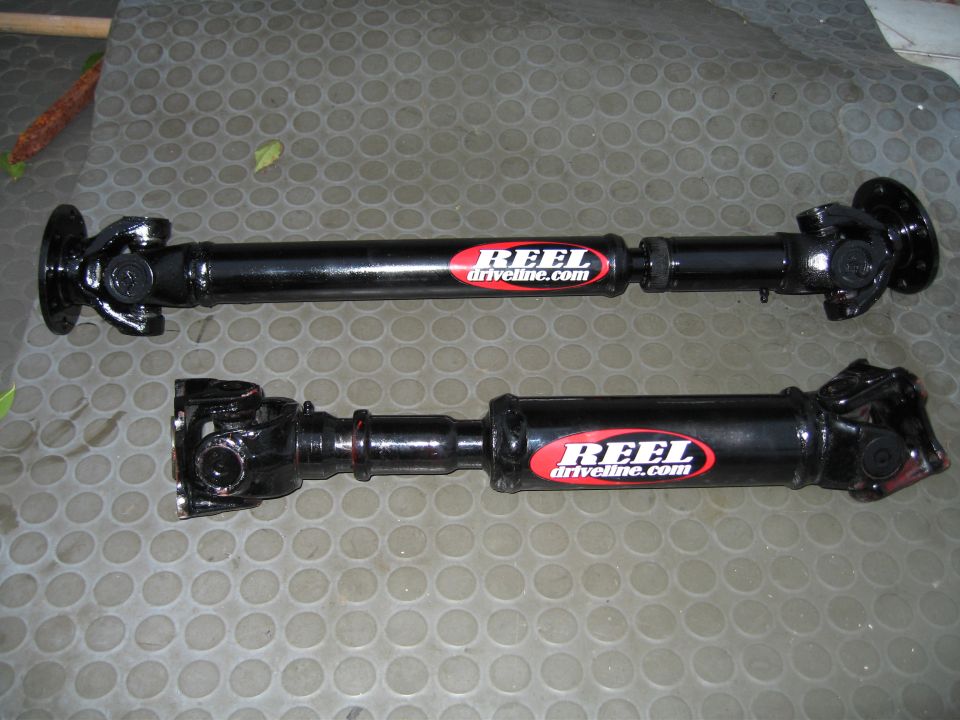 Two black driveline driveshafts with REEL Driveline stickers lying on a rubber mat