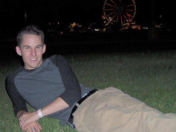 Man lying on grass at night, Ferris wheel illuminated in the background