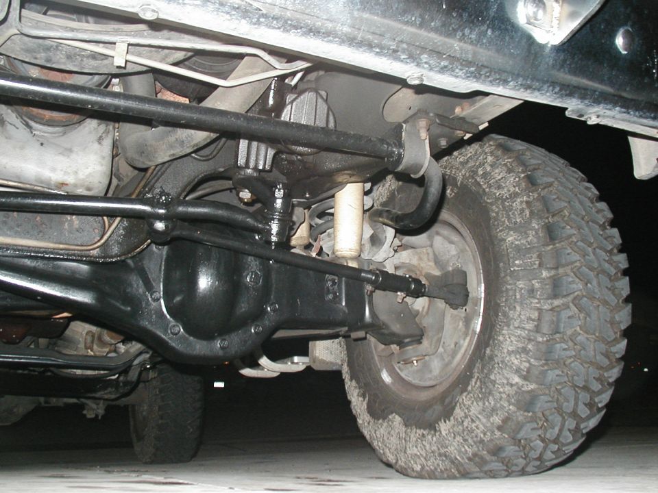 Underbody view of a 4x4 front solid axle, differential, steering linkage and mud-terrain tire.