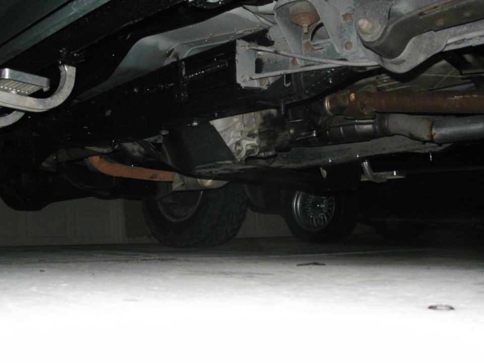 Undercarriage of a vehicle showing the transmission, exhaust system, and tires. The frame is painted black