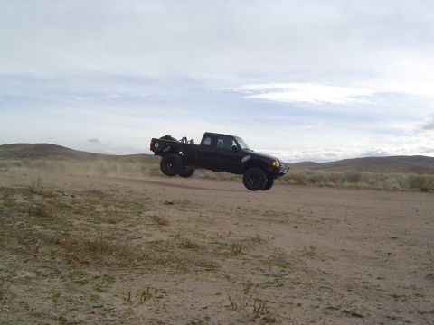 1985 Ford Ranger - This 1985 Ford Ranger is captured mid-air during a jump over a dusty dirt road in a desert landscape.