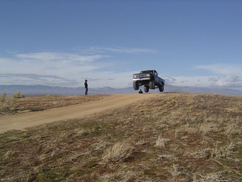 1985 Ford Ranger - A truck is captured mid-air as it crests a hill, with a lone figure observing the jump.