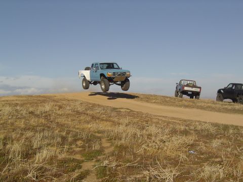 1985 Ford Ranger - A modified pickup truck soars through the air, with other trucks following on a dirt road.