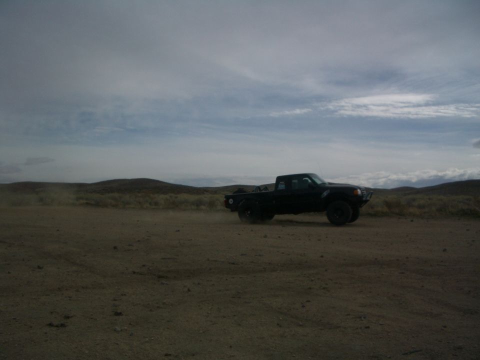 Black pickup truck driving on a dirt road with hills in the background