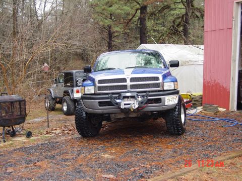 1995 Dodge 1500 - A blue Dodge pickup truck with a winch is parked in a yard next to a red building, with a Jeep in the background.