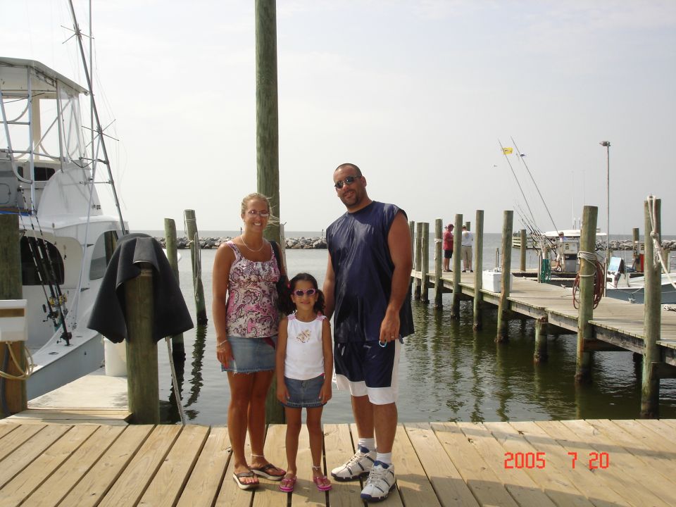 Family of three posing on a wooden marina dock near boats
