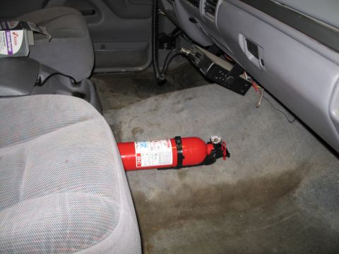 1995 Ford Bronco - A red fire extinguisher is secured to the floor of a vehicle's passenger side.