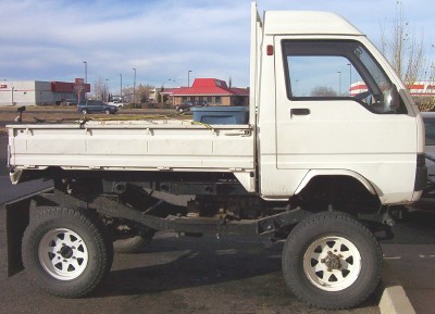 1995 Ford Bronco - A white flatbed truck is viewed from the side, showing its lifted chassis and aftermarket wheels.