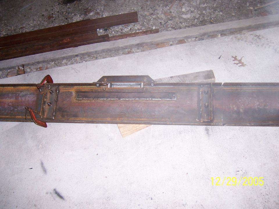 Welded steel frame rail section with bracket plates lying on a concrete garage floor