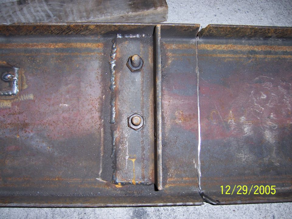 Rusty steel frame section with welded plate, two bolts with hex nuts, and a spliced seam; dated 12/29/2005