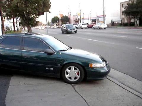 1993 Ford Taurus - A green sedan is parked on the side of a street with other cars in the background.