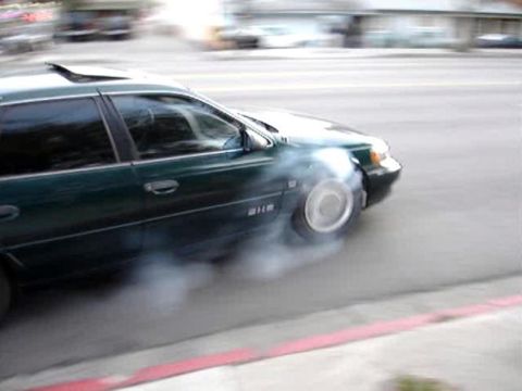 1993 Ford Taurus - A green sedan is performing a burnout, with smoke billowing from its tires on a city street.