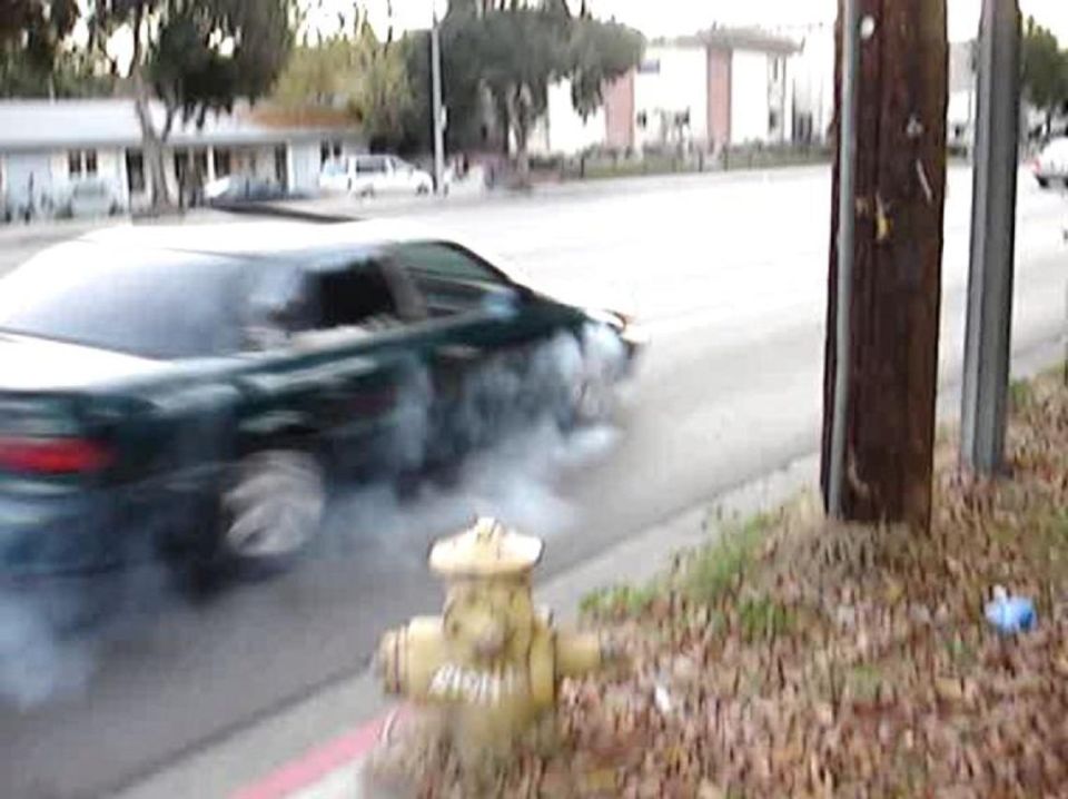 Dark green sedan performing a burnout, emitting smoke from rear tires