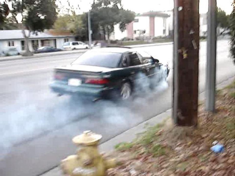 Dark green 1993 Ford Taurus doing a burnout, rear view