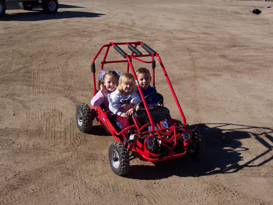 red go-kart with three kids in it, parked on dirt