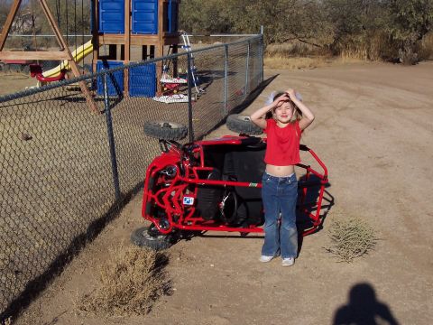 1981 Ford F-150 - A child stands by an overturned red go-kart near a playground fence.