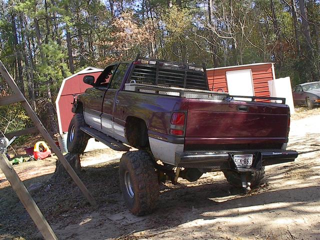Maroon 2001 Dodge 1500 pickup truck with large tires, parked on uneven ground near a red shed