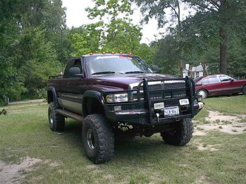 2001 Dodge 1500 - Lifted Dodge pickup truck with bull bar and aftermarket wheels is parked on grass with a red sedan in the background.