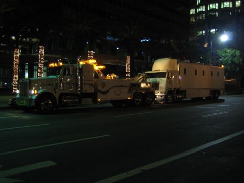 1968 Ford Mustang - A tow truck is seen at night, towing a large box truck on a city street.