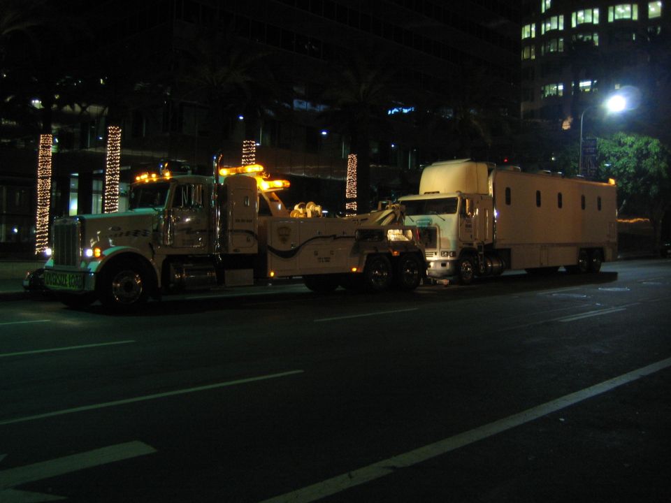 Tow truck with flashing lights is towing a large box truck at night