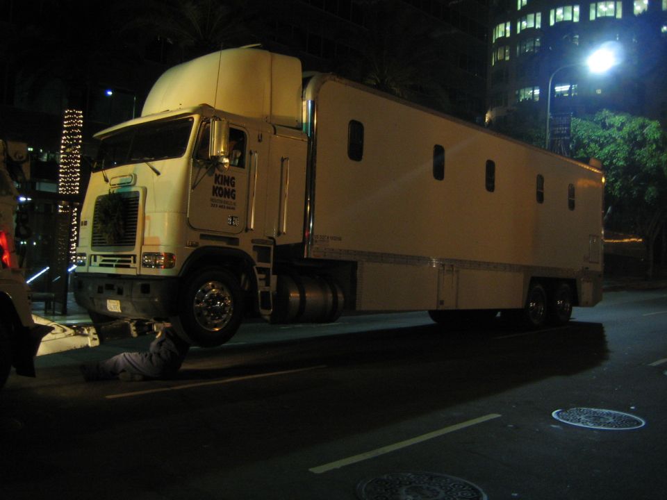 White semi-truck with 'KING KONG' logo on the door, a person is lying underneath it on the road