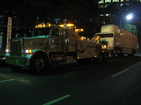 1968 Ford Mustang - A tow truck transports a trailer on a city street at night, with building lights in the background.