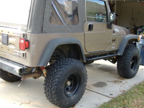 2004 Jeep Wrangler - A tan 2004 Jeep Wrangler is shown from a three-quarter front angle, modified with large tires and a lift kit.