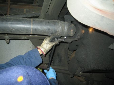 1968 Ford Mustang - A mechanic is shown working on the undercarriage of a vehicle, focusing on the driveshaft assembly.