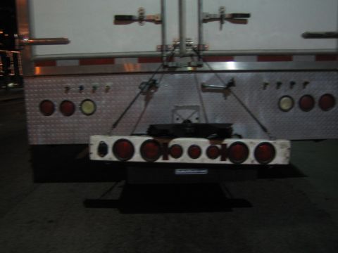 1968 Ford Mustang - The rear of a large trailer is shown, multiple red lights and reflective diamond plate.
