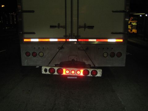 1968 Ford Mustang - The rear of a semi-trailer truck is visible at night, multiple red taillights and reflective safety tape.