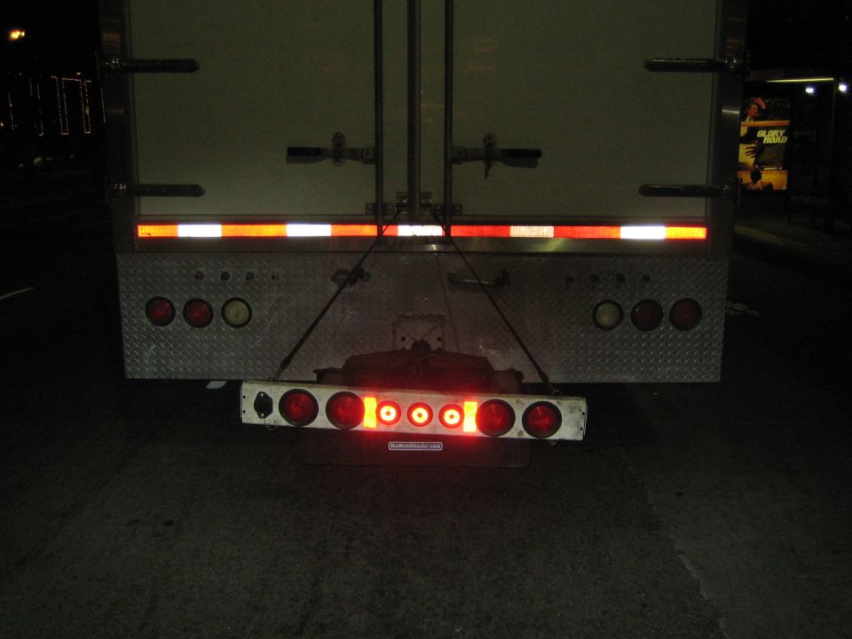 Rear of a semi-trailer truck with red taillights and reflective tape