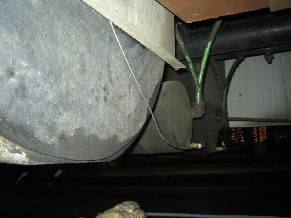 Undercarriage of a vehicle showing two large grey tanks, green hoses, and black pipes