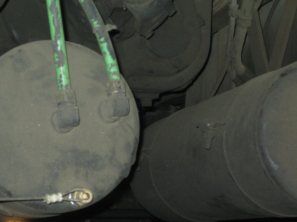 Undercarriage of a truck showing two large air tanks and green hoses