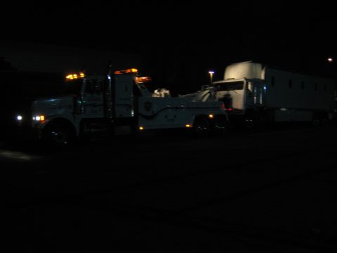 1968 Ford Mustang - A tow truck is seen at night, towing a trailer. The scene appears to be a breakdown or recovery operation.