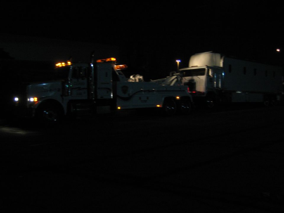 Tow truck with flashing lights towing a trailer at night