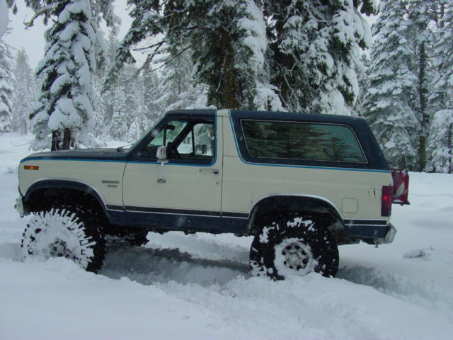 1986 Ford Bronco driving through deep snow, side view