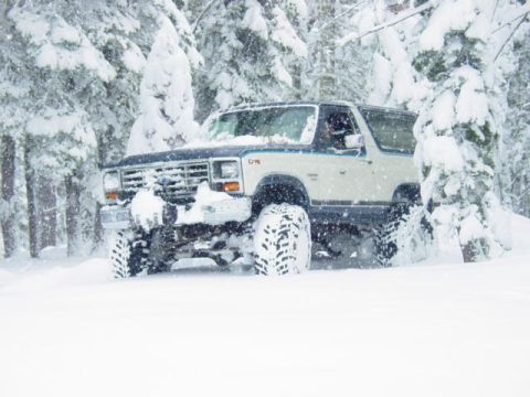 1986 Ford Bronco - A lifted Ford Bronco navigates a snowy forest trail during a winter storm.