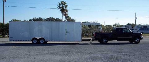 2000 Ford F-250 - Black 2000 Ford F-250 pickup truck is seen towing a large white enclosed trailer.