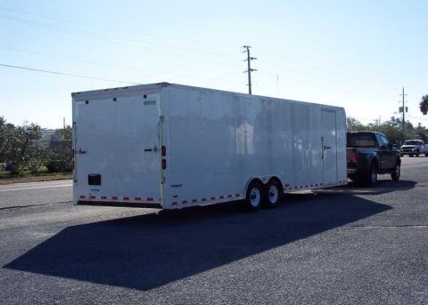 2000 Ford F-250 - A pickup truck tows a large white enclosed cargo trailer down a road under a clear blue sky.