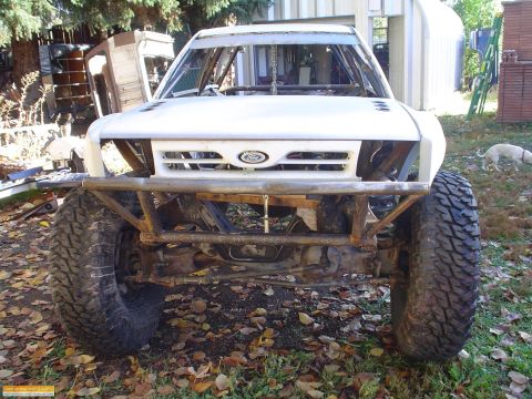 1991 Ford Bronco - Front view of a white off-road truck with a prominent custom bumper and large tires. The Ford emblem is visible on the grille.