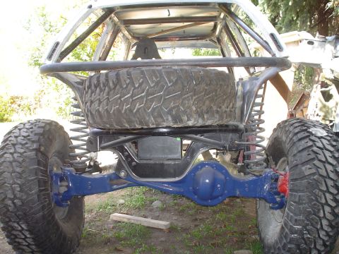 1981 Ford F-150 - Custom off-road vehicle rear axle and suspension system with a large spare tire mounted above.