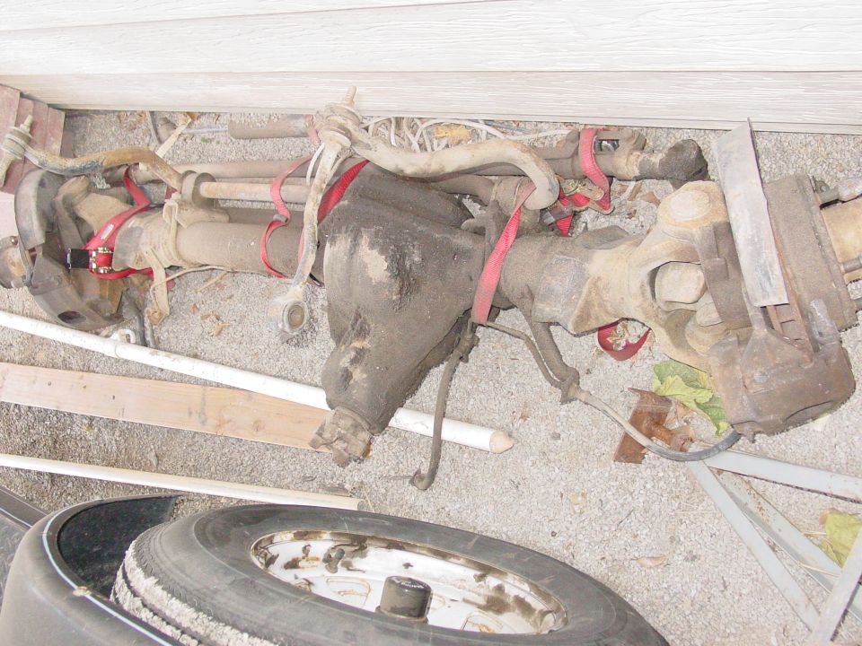 Used front axle assembly with differential and brake calipers on gravel ground