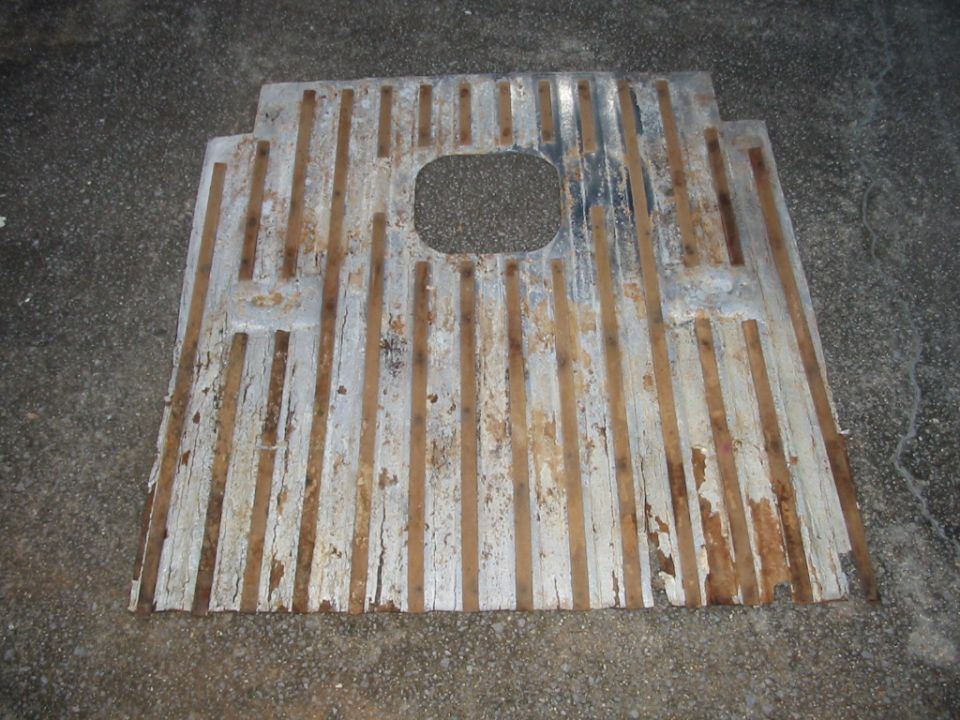 Rusty white-painted ribbed metal floor panel with center cutout, lying on wet pavement