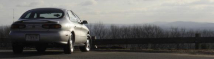 1999 Ford Taurus - A silver 1999 Ford Taurus is seen from the rear on a road with a scenic mountain backdrop.