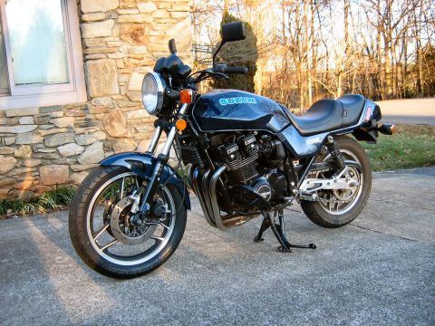 1985 Ford LTD Crown Victoria - Dark blue Suzuki standard motorcycle on its centerstand in a driveway, shown from the front three-quarter with an air-cooled inline-four en…