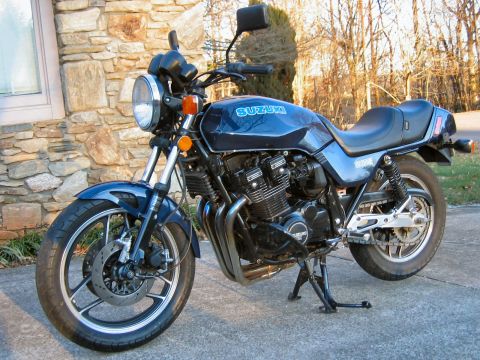 1985 Ford LTD Crown Victoria - A dark blue Suzuki GS1100E standard/naked motorcycle with an air-cooled inline-four engine, chrome front fork, round headlight, and dual fr…