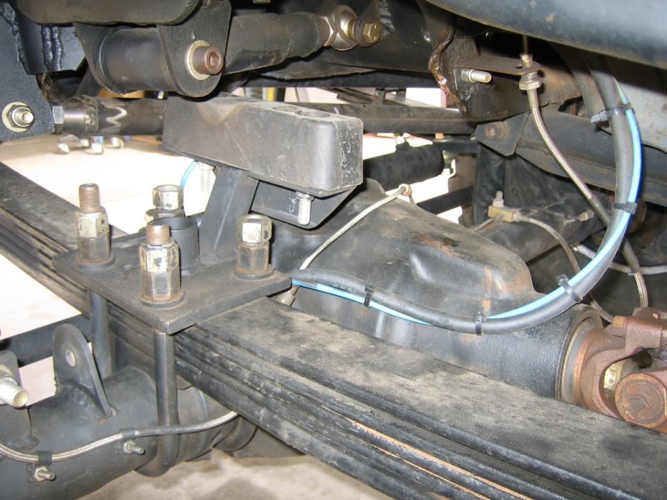 Rear axle assembly with leaf springs, U-bolts, and driveshaft. Black rubber bump stop above axle