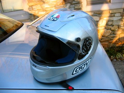 1985 Ford LTD Crown Victoria - A silver AGV motorcycle helmet sits on the hood of a car, with a stone wall in the background.