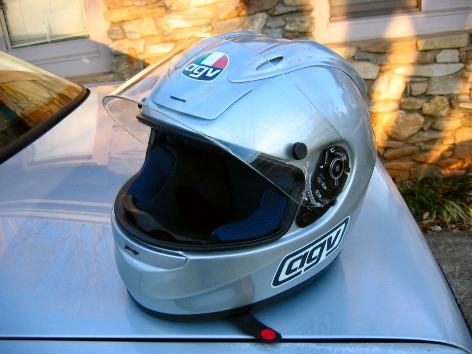 Silver AGV motorcycle helmet with clear visor resting on a car hood